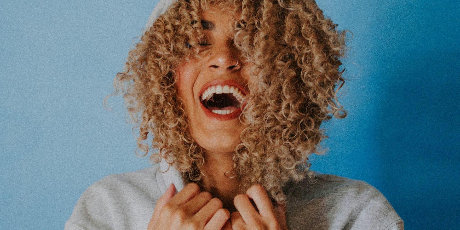 Une femme qui utilise une crème pour les cheveux bouclés rigole